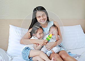 Young Asian mother with her daughter and baby boy relaxing and playing on the bed at the morning