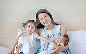 Young Asian mother with her daughter and baby boy relaxing and playing on the bed at the morning