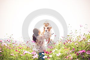 Young asian mother with her pretty curly daughter are walking in spring garden with pink blossom roses flowers, sunset time.