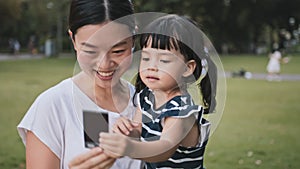 Young Asian mother hold cute daughter, look at polaroid photo picture with smile. Mom kid love relationship
