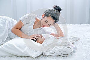 Young Asian mother lie on white bed and take care her newborn baby