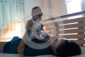 Young asian mother lying down on bed and playing with her baby daughter to relax together in bedroom