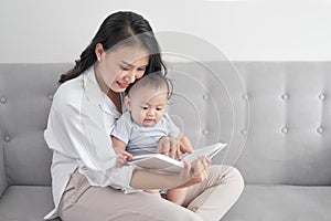 Young asian mother reading book to baby. Sweet moment.