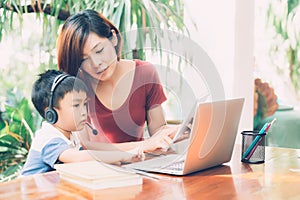 Young asian mother and son using laptop computer and tablet for study and learn together at home.