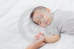 Young asian mother touch hand of little baby girl with tender on bed in the bedroom.