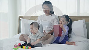 Young asian mother working at home online to internet with laptop computer and daughter looking tablet.