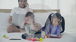 Young asian mother working at home online to internet with laptop computer and talking phone and daughter looking tablet.