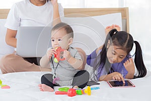 Young asian mother working at home online to internet with laptop computer and talking phone and daughter looking tablet.