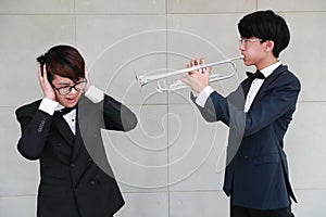 Young musician man wearing black suit making too loud music and annoying from trumpet to his friend