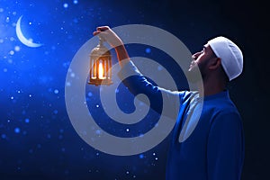 Young asian muslim man with beard hold arabic lantern looking at beautiful blue night