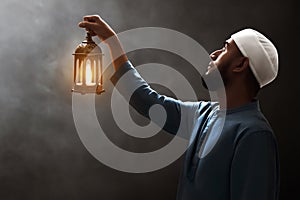 Young asian muslim man with beard holding arabic lantern looking up on dark backgrounds at night