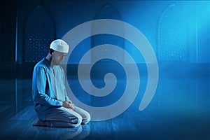 Young asian muslim man with beard pray in the mosque window arch at dark night