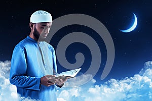 Young asian muslim man with beard read holy book quran at blue night sky with stars and crescent moon