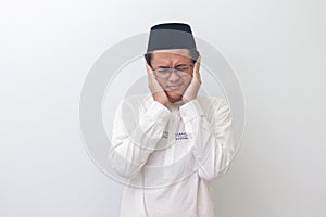 young Asian muslim man covering ears with fingers with annoyed expression for the noise of loud music and sound.