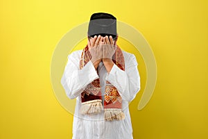 Young Asian Muslim man feel sad with covering his face with hands. Copy space concept