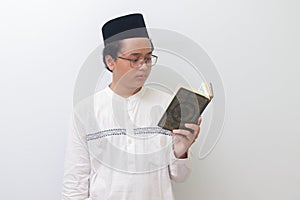 Joven asiático hombre lectura a santo un libro de Corán en serio. imagen en blanco 