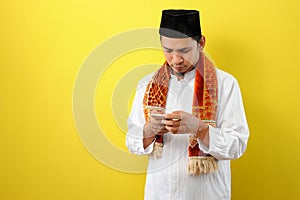 Young Asian Muslim man wearing moslim clothes holding mobile phone look at phone screen