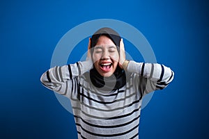 Young asian muslim woman in hijab close her ear isolated on blue background