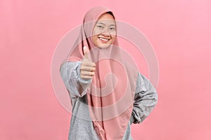 Young Asian Muslim woman showing thumb up against pink colour background