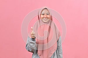 Young Asian Muslim woman showing thumb up against pink colour background