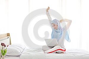 Young asian muslim woman using laptop sitting on bed in bedroom. photo