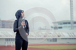 A young asian Muslim woman wearing a black hijab is exercising and running at an outdoor stadium in the morning.