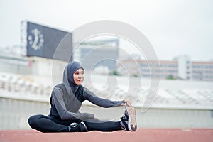 A young asian Muslim woman wearing a black hijab is exercising and running at an outdoor stadium in the morning.