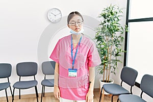 Young asian nurse woman at medical waiting room looking sleepy and tired, exhausted for fatigue and hangover, lazy eyes in the