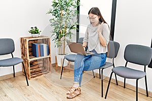 Young asian nurse woman sitting at waiting room using laptop celebrating victory with happy smile and winner expression with