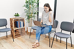 Young asian nurse woman sitting at waiting room using laptop screaming proud, celebrating victory and success very excited with