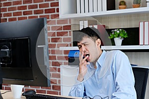 Young asian office man yawning while working on paperwork and computer, Exhausted creative businessman take a break from work at