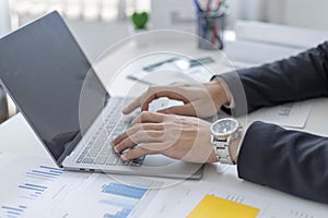 Young Asian office worker presses he finger on a laptop keyboard to analyze financial data and summarize her work in a private off