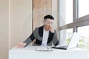 Young asian office worker suffering from headache at work in the office drinks medicine pill with water.