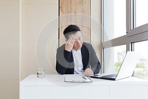 Young asian office worker suffering from headache at work in the office drinks medicine pill with water.