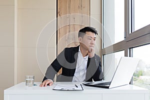 Young asian office worker suffering from headache at work in the office drinks medicine pill with water. Sick man in a suit