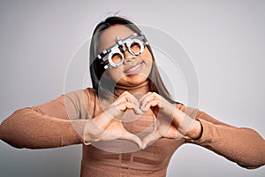 Young asian optical girl controlling eyesight using optometry glasses over white background smiling in love showing heart symbol