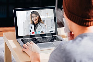 Young Asian patient with sickness using laptop to video call conferencing with female doctor from home. Medical