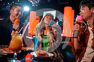 Young asian people having fun while singing karaoke on night party at club
