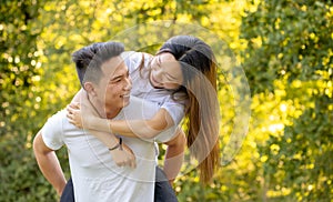 Young asian people in love piggybacking at city park in a sunny summer day