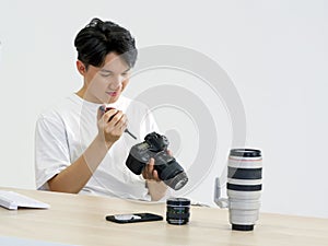 Young asian photographer is cleaning the camera screen and body with a blower camera for cleaning on his desk