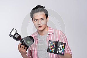 Young asian photographer holding digital camera and color checker card, while working in studio