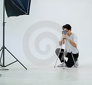 Young asian photographer looks through the viewfinder while shooting with the camera. Working atmosphere in the photo studio