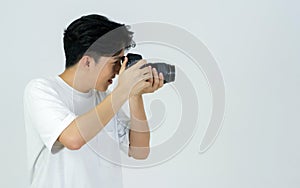 Young asian photographer in white t-shirt looks through the viewfinder while shooting with the camera. Working atmosphere in the