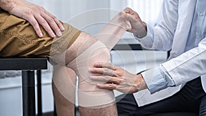 Young asian physiotherapist bandaging knee of man patient with in injury