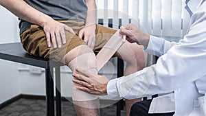 Young asian physiotherapist bandaging knee of man patient with in injury