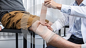 Young asian physiotherapist bandaging knee of man patient with in injury