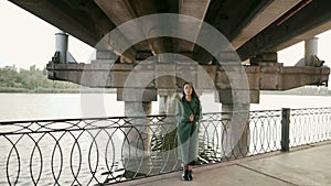 Young asian posing looking to camera staying under bridge on river embankment