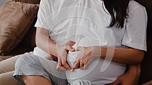 Young Asian Pregnant couple making heart sign holding belly. Mom and Dad feeling happy smiling peaceful while take care baby,