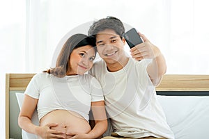 Young Asian pregnant woman with husband on the white bed in the house