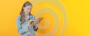 Young asian pretty woman smiling using mobile tablet computer on copy space area on yellow panoramic wide background, business fin